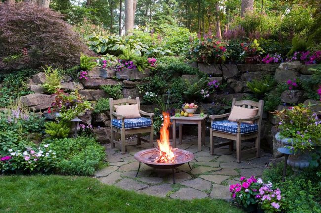Уютное патио в саду с красивым ландшафтным дизайном и обилием цветущих растений